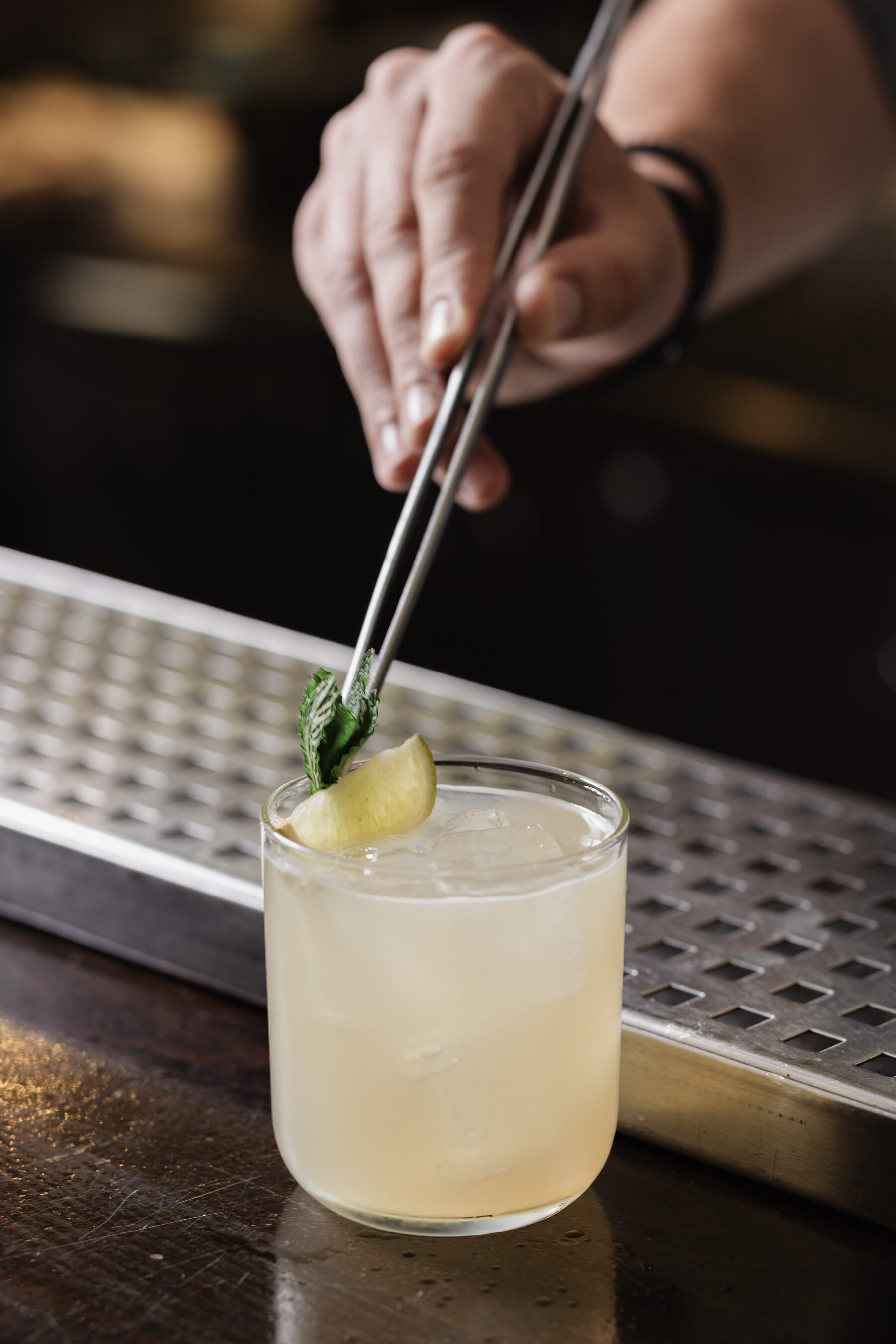 A Madison bartender placing a mint leaf on a citrus cocktail with tweezers