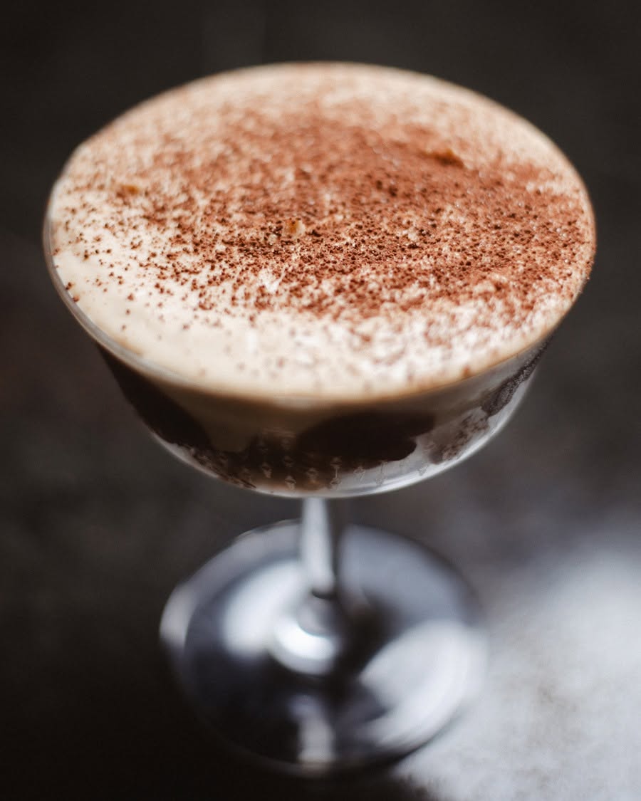 A dark cocktail under a dense cocoa-dusted foam