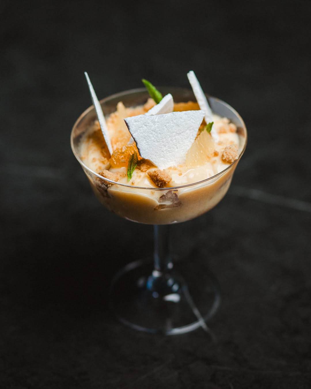 A layered dessert in a coupe, white chocolate shards leaning into cream