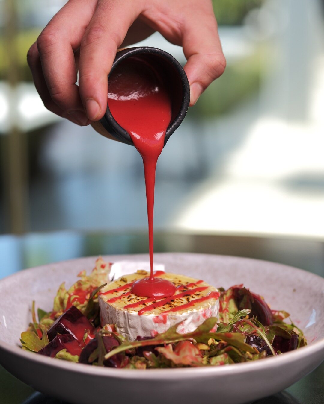Grilled camembert dressed with beetroot coulis over leaves and candied nuts