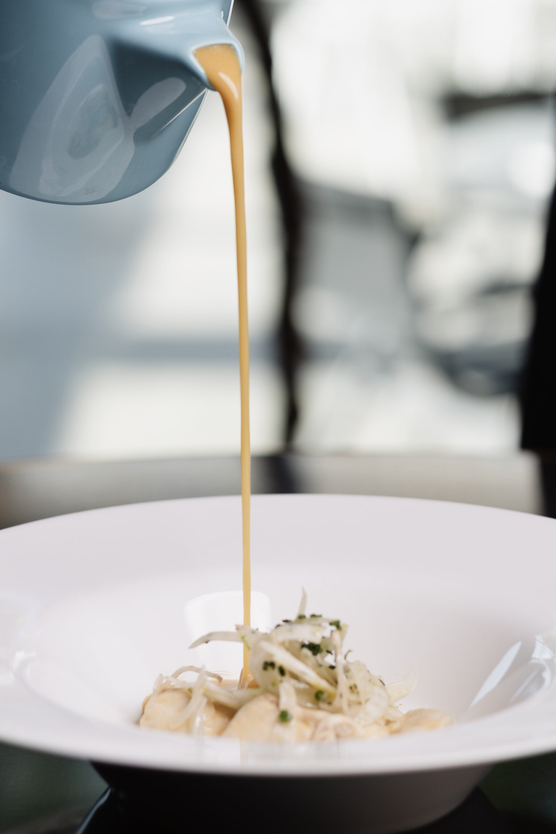 Shellfish bisque poured over gnocchi and shaved fennel in a wide white bowl