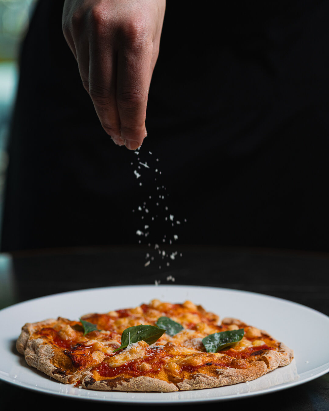 Grated cheese falling over a freshly baked pizza in low light