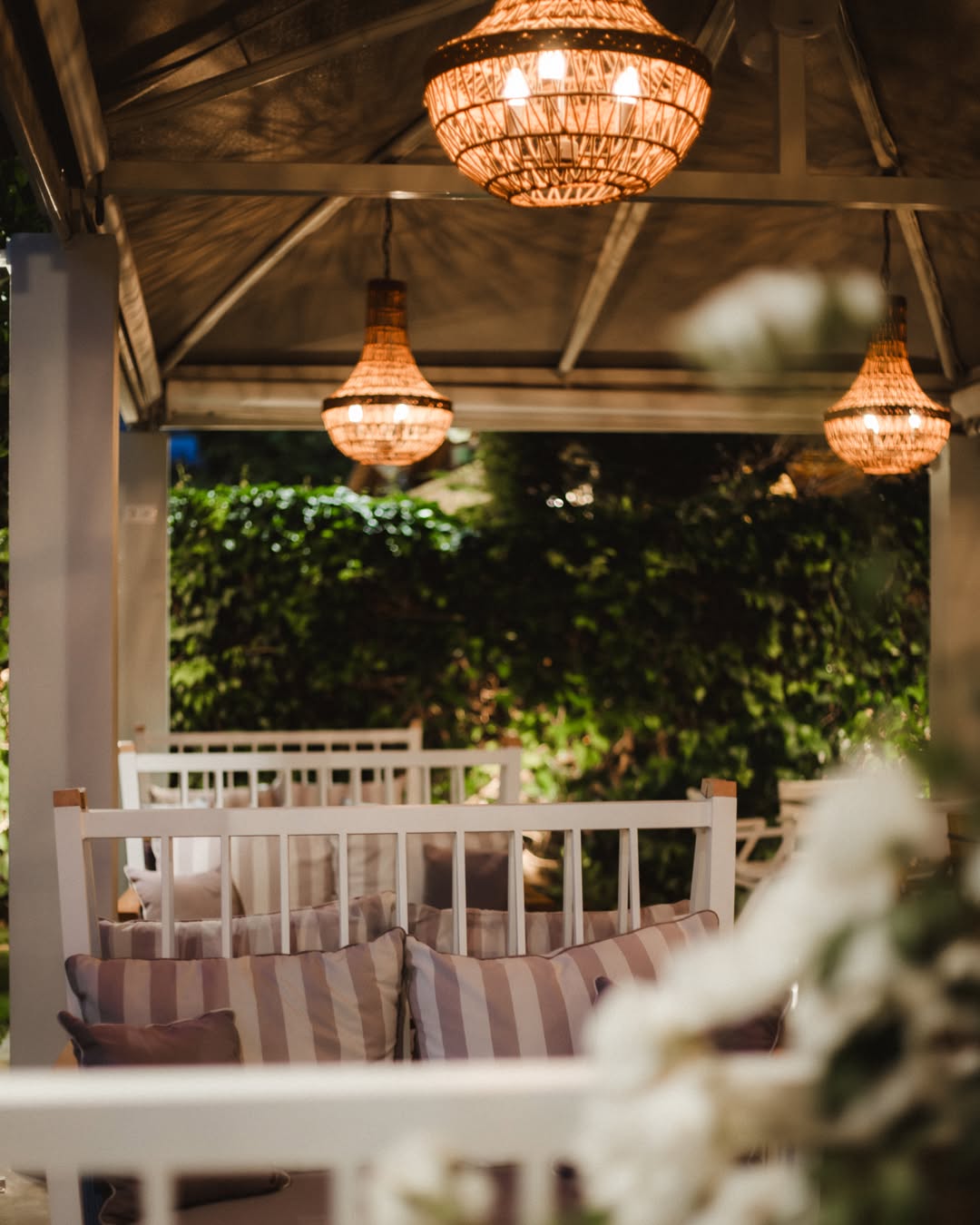A Madison pavilion at dusk — chandeliers lit over striped sofas, the garden dark behind