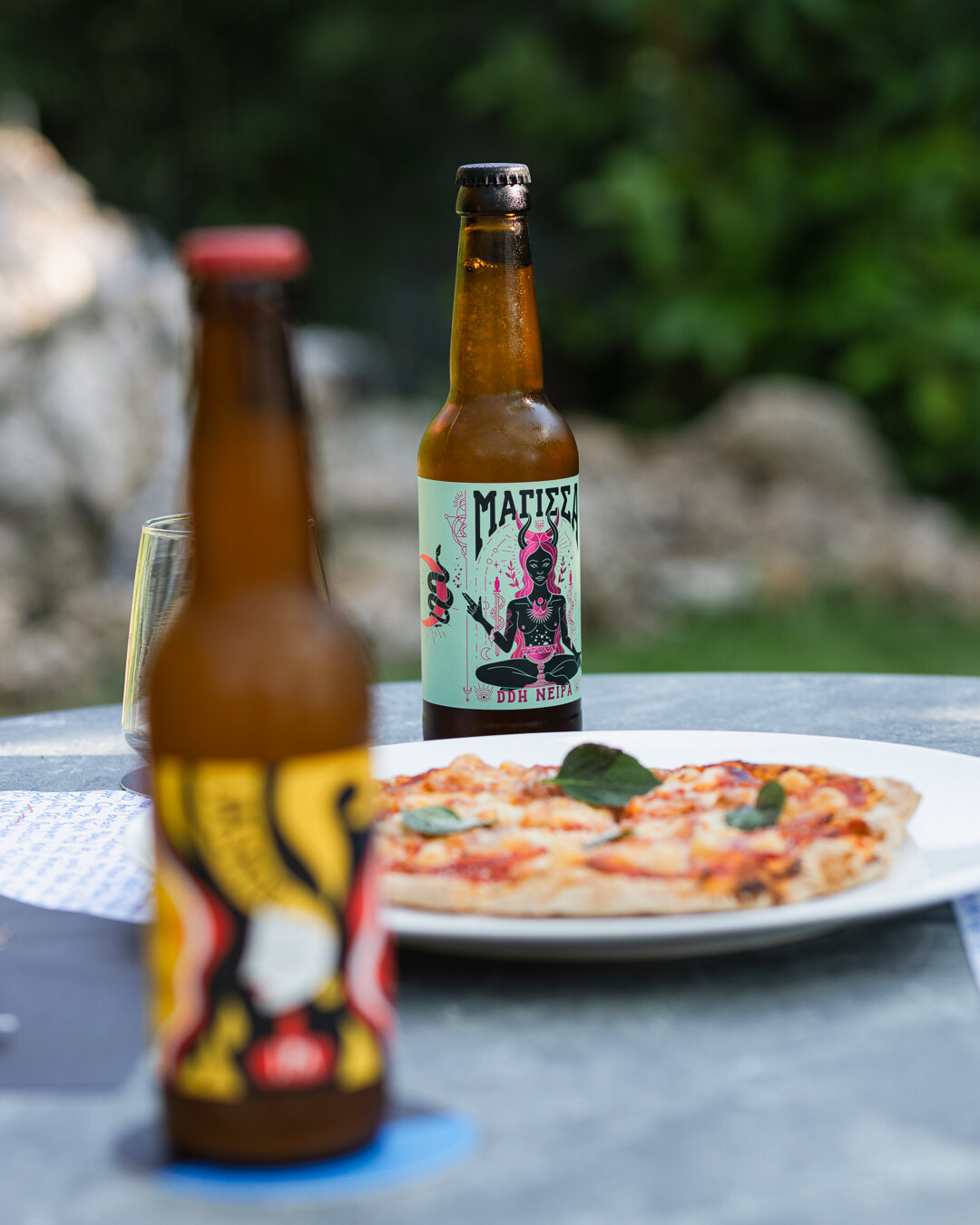 Chilled Greek craft beers beside a pizza on a garden table at Madison